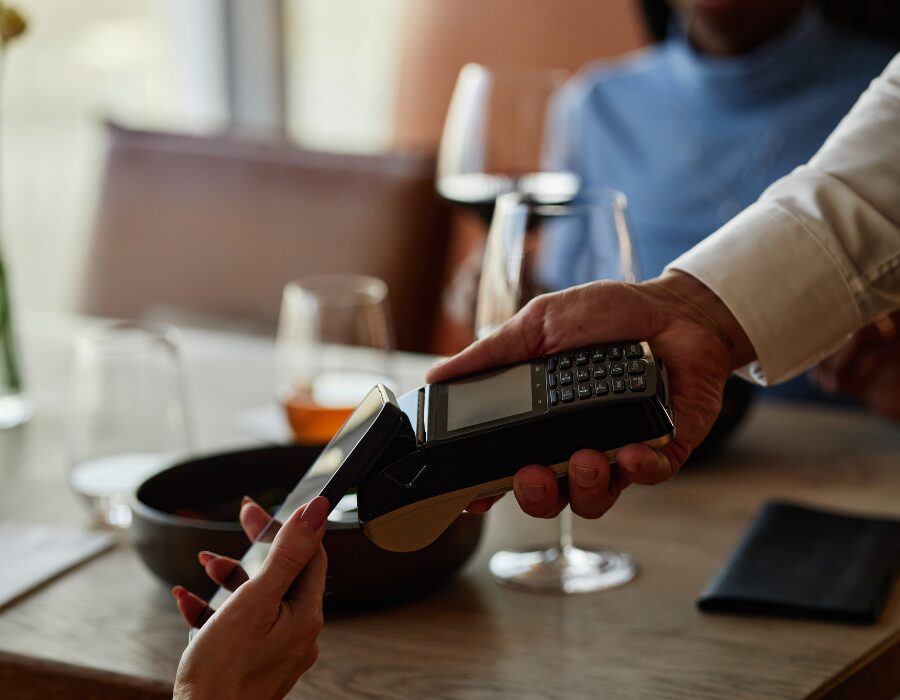 a customer with their card tapping an wireless payment device at a table with empty wine glasses