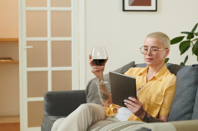 woman relaxing on couch in her living room with a tablet in her hand and a glass of red wine in the other